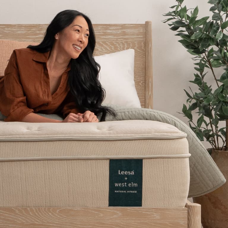 Leesa natural mattress with female model on the bed with pillows and soft bedding